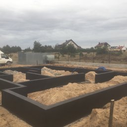 USŁUGI OGÓLNOBUDOWLANE ED-BUD EDWIN SZEFKA - Zalane fundamenty domu jednorodzinnego w Leśniewie, widoczne zbrojenia i piasek wewnątrz, w tle zabudowa jednorodzinna i pochmurne niebo.