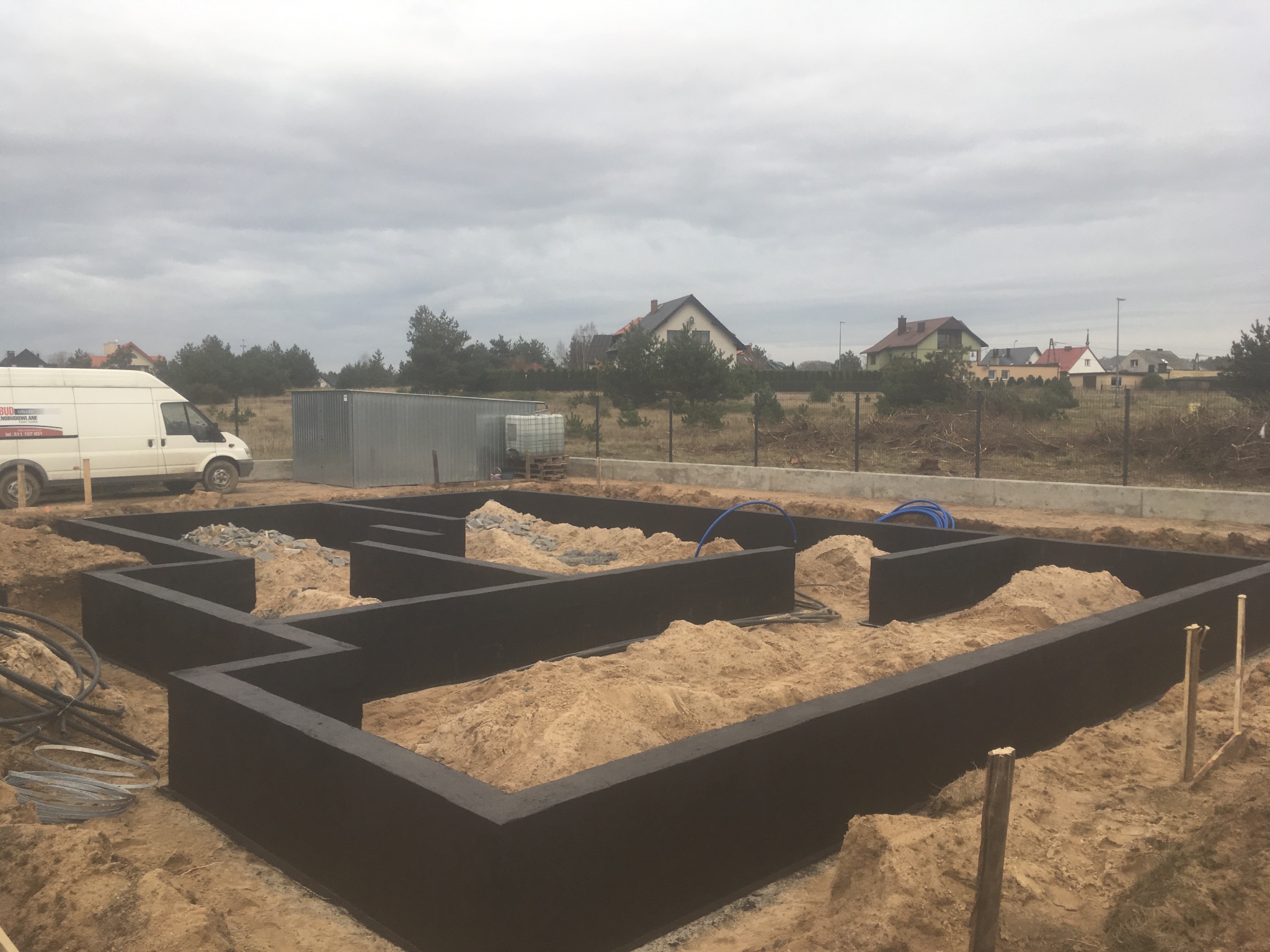Zalane fundamenty domu jednorodzinnego w Leśniewie, widoczne zbrojenia i piasek wewnątrz, w tle zabudowa jednorodzinna i pochmurne niebo.