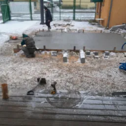 Wylewka betonowa na przygotowanym terenie w zimowej scenerii, widoczne szalunki, narzędzia i pracownik w trakcie pracy.