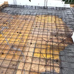 Przygotowanie zbrojenia na deskowaniu pod wylewkę betonową, widoczne fragmenty wylanego betonu, budynek w tle.