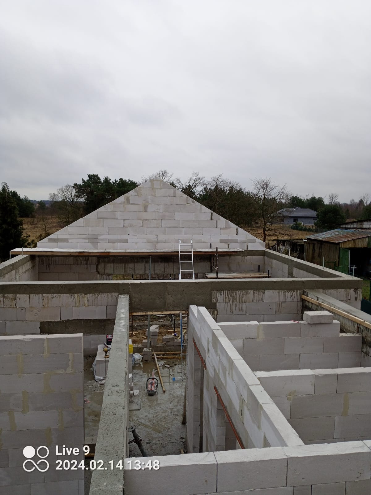 Budowa domu z bloczków betonu komórkowego Ytong, widok na wznoszone ściany parteru i szczyt dachu, drabina oparta o ścianę, narzędzia na mokrej posadzce.