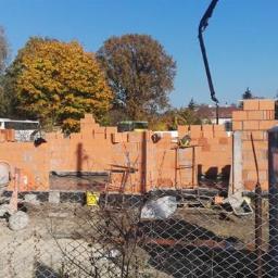 Elinmar Invest Sp. z o.o. - Budowa domu jednorodzinnego w trakcie wznoszenia murów z czerwonej cegły, widoczna betoniarka, pompa do betonu i przenośna toaleta ToiToi.