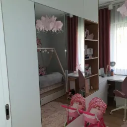 Biała szafa z lustrzanymi drzwiami przesuwnymi w pokoju dziecięcym, odbijająca łóżko tipi, lampę w kształcie chmury i różowy wózek dla lalek.