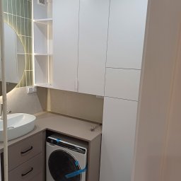 MAG BUD Jarosław Węgrzyn - Nowoczesna łazienka z zabudową meblową: białe szafki wiszące, szara zabudowa pralki i umywalki z szufladami, okrągłe lustro z podświetleniem.