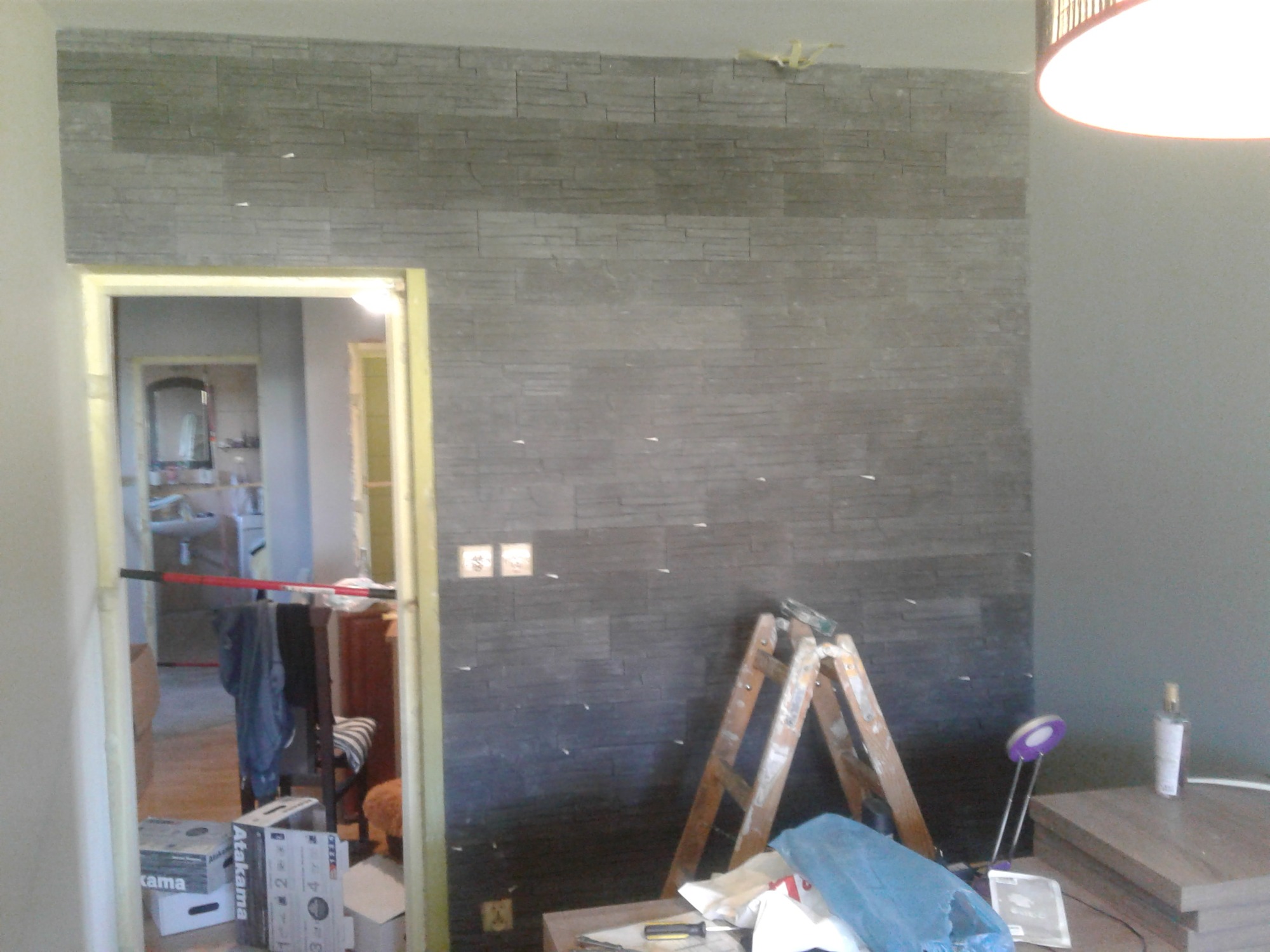 Montaż dekoracyjnej ściany z płytek imitujących kamień, widoczne poziomice, drabina i inne narzędzia w trakcie pracy.