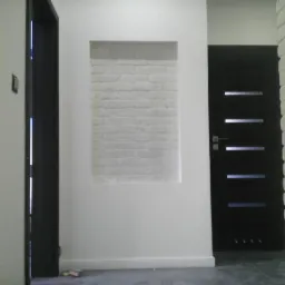 Wnęka z białej cegły w ścianie, obok czarne drzwi z przeszkleniami i drugie drzwi po lewej stronie. Wykończenie wnętrza w nowoczesnym stylu.