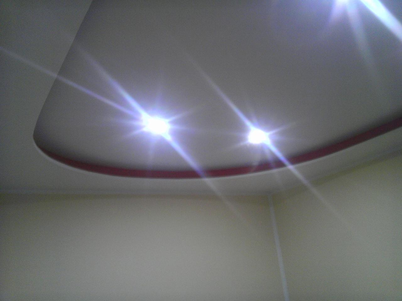 Nowoczesny sufit podwieszany z dwoma punktami świetlnymi, wykończony czerwoną listwą, widok z perspektywy narożnika pomieszczenia.