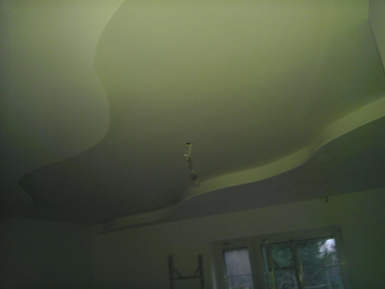 Falisty, podwieszany sufit z płyt kartonowo-gipsowych, oświetlenie punktowe, widok z dołu, okno w tle. Nowoczesny design wnętrza.