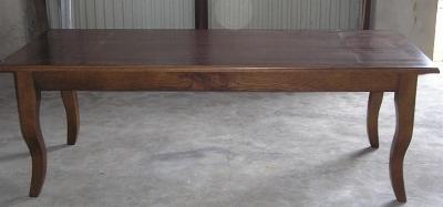 Stół drewniany z giętymi nogami w stylu ludwikowskim, wykonany z ciemnego drewna, widoczny na szarym, betonowym tle.