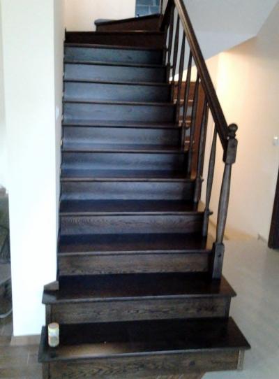 Ciemne, drewniane schody z balustradą w jasnym wnętrzu, widoczne z dołu, z delikatnym oświetleniem.