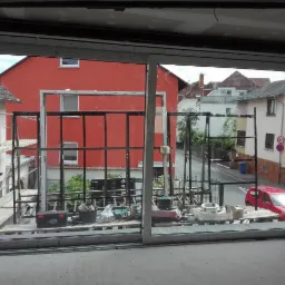 Widok z wnętrza na rusztowanie przed czerwonym budynkiem, widziany przez nowo zamontowane okno przesuwne z widocznymi narzędziami na zewnątrz.