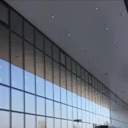 Fasada budynku biurowego z rzędem dużych okien, odbijających niebo, oświetlona szeregiem wpuszczanych lamp sufitowych.