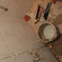 Układanie płytek w łazience: widok na świeżo ułożone płytki z krzyżykami dystansowymi, wiadro z zaprawą, narzędzia i fragment podłogi w trakcie prac wykończeniowych.