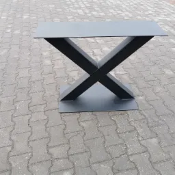 Metalowa podstawa stołu z nogami w kształcie litery X, pomalowana na szaro, sfotografowana na szarej kostce brukowej.