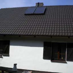 Dwa kolektory słoneczne na brązowym dachu domu z białymi ścianami i drewnianymi okiennicami. Na stole dzbanek i kamienie.