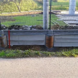 Montaż ogrodzenia panelowego z podmurówką betonową i słupkami, widoczny pracownik w odzieży roboczej oraz poziomica oparta o słupek.