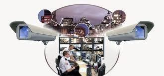 Schematyczne ujęcie systemu monitoringu wizyjnego: dwie kamery przemysłowe na tle nocnej panoramy miasta, połączone z centrum monitoringu obsługiwanym przez dwóch operatorów.