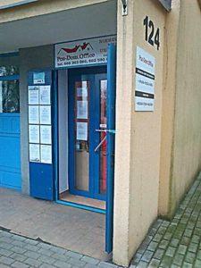 Wejście do biura nieruchomości z niebieskimi drzwiami i tabliczką informacyjną na ścianie, numer budynku 124.