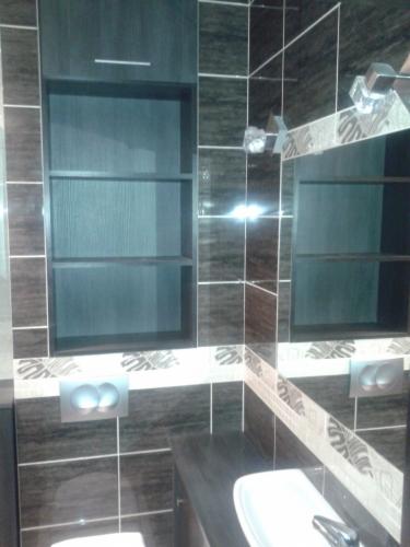 Wykończona łazienka z ciemnymi, wzorzystymi płytkami, zabudową nad toaletą i lustrem. Widoczna umywalka i bateria. Detale wykończenia.