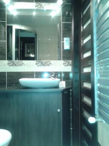 Nowoczesna łazienka z umywalką nablatową, ciemnymi płytkami i grzejnikiem drabinkowym. W lustrze odbija się kabina prysznicowa.