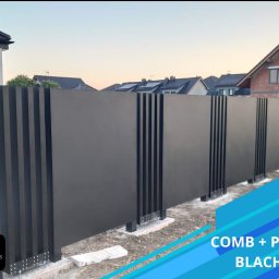 EURO-FENCES Slawomir Sulkowski - Nowoczesne ogrodzenie panelowe z pełnej blachy z elementami dekoracyjnymi w postaci wąskich pionowych listew, widoczne elementy montażowe do podłoża, w tle zabudowa jednorodzinna.