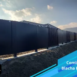 Nowoczesne ogrodzenie z czarnych paneli pełnych i ażurowych, na betonowej podmurówce, z widokiem na dom i wzgórza w tle.