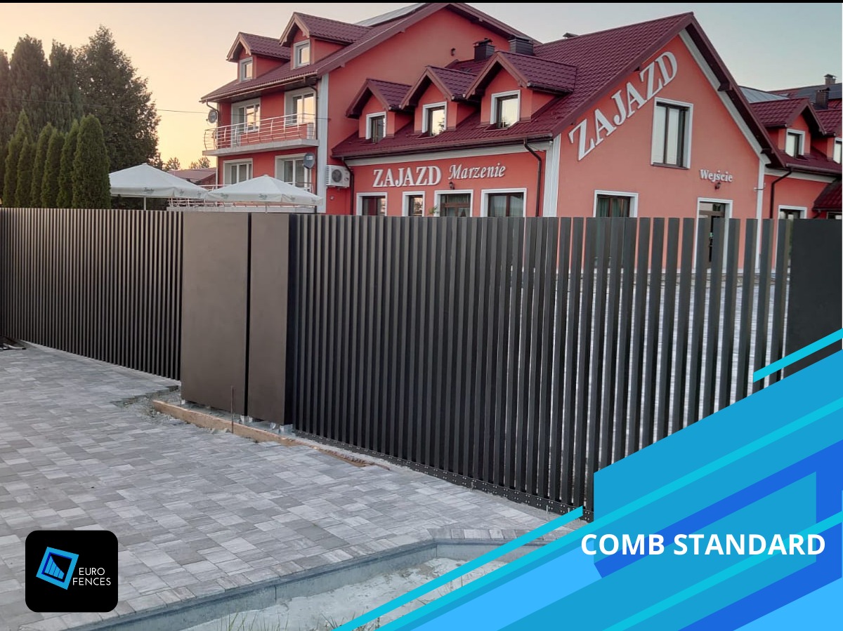 Nowoczesne, pionowe, metalowe ogrodzenie w kolorze grafitowym przed budynkiem ZAJAZD Marzenie, z widoczną kostką brukową i fragmentem logo firmy EURO FENCES.