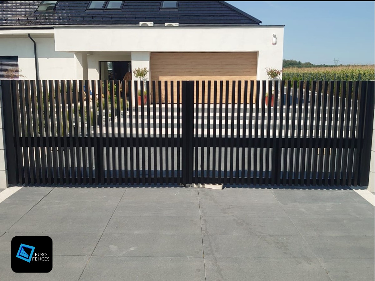 Nowoczesna, czarna brama wjazdowa z pionowych profili na tle domu z garażem i zagospodarowanym terenem.