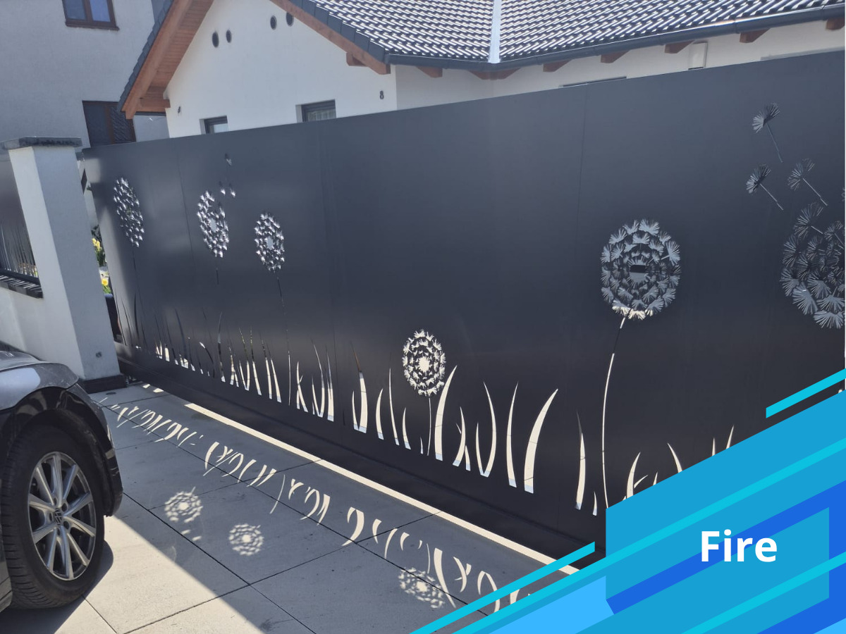 Czarna brama przesuwna z ażurowym wzorem dmuchawców, oświetlona słońcem, z fragmentem samochodu w kadrze. Nowoczesny design bramy.