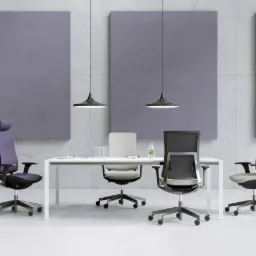 Nowoczesna sala konferencyjna z czterema krzesłami biurowymi o różnej kolorystyce i designie, białym stołem, betonową ścianą z trzema szarymi panelami akustycznymi i dwoma wiszącymi lampami w stylu...