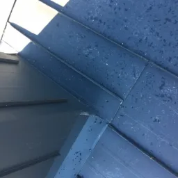 Fragment nowo położonego, ciemnego dachu z blachy na rąbek stojący z widocznymi śladami po deszczu.