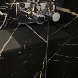 Zakład instalacyjny Pazoła Janusz - Błyszcząca, chromowana bateria umywalkowa z dwoma kurkami zamontowana na ścianie z czarnego marmuru z białymi żyłami.