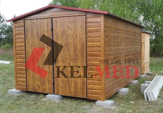 Gotowy, brązowy garaż blaszany z dwuskrzydłowymi drzwiami, imitujący drewno, osadzony na betonowych bloczkach, z widocznym logo firmy na drzwiach i małą dobudówką z boku.