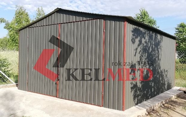Szary garaż blaszany z czerwonymi obramowaniami, postawiony na betonowej wylewce, z widocznym logo firmy producenta z rokiem założenia 1993.