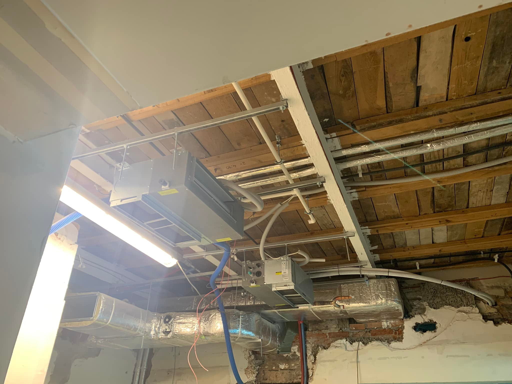 Montaż klimatyzacji i wentylacji w budynku: widoczne kanały wentylacyjne, jednostki klimatyzacyjne pod sufitem, instalacje w trakcie podłączania, surowy stan wykończenia.