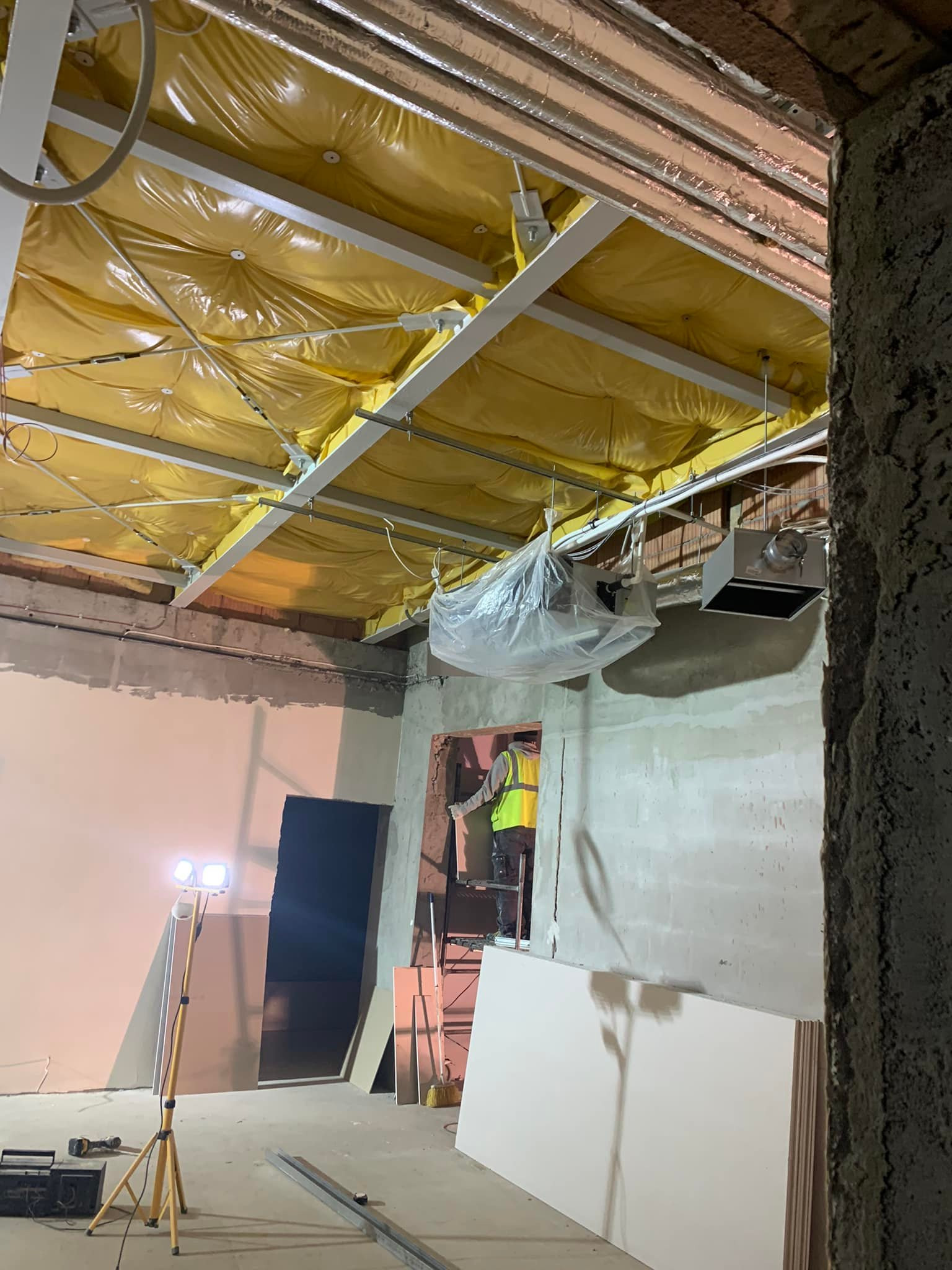 Montaż instalacji wentylacyjnej: widok na sufit z izolacją w folii, pracownik w kamizelce, lampa budowlana. Prace instalacyjne w budynku komercyjnym.