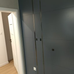 Baranski - Szara, zabudowana szafa wnękowa z metalowymi wstawkami i kwadratowymi uchwytami, widoczny biały futryna drzwi i fragment podłogi.