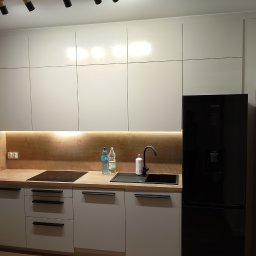 Baranski - Nowoczesna kuchnia z białymi szafkami, drewnianym blatem, czarną armaturą i lodówką Samsung, oświetlona listwą LED pod szafkami wiszącymi i reflektorami na suficie.