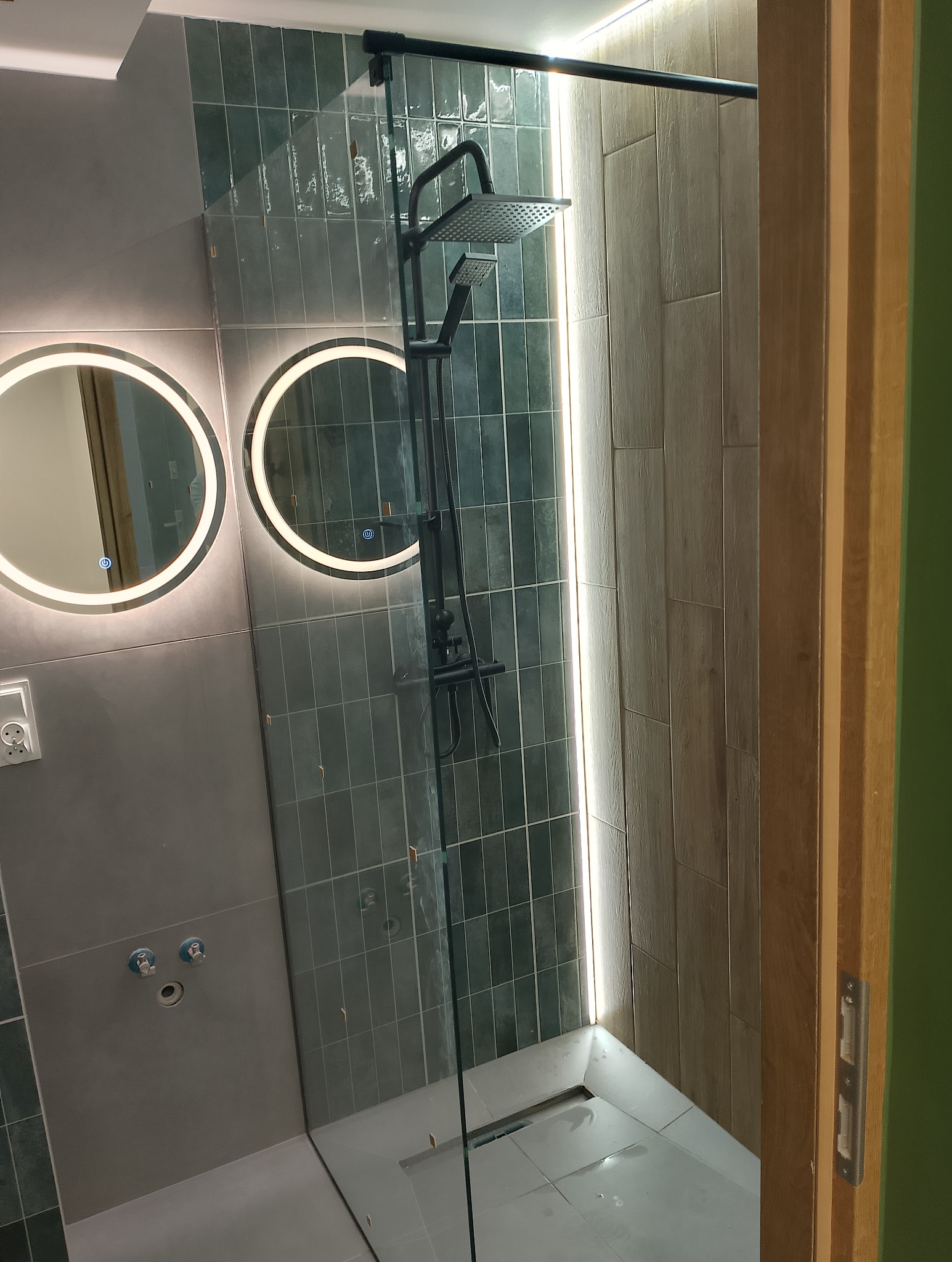 Nowoczesna kabina prysznicowa typu walk-in z czarną armaturą, podświetlanymi okrągłymi lustrami i płytkami w odcieniach szarości i beżu.