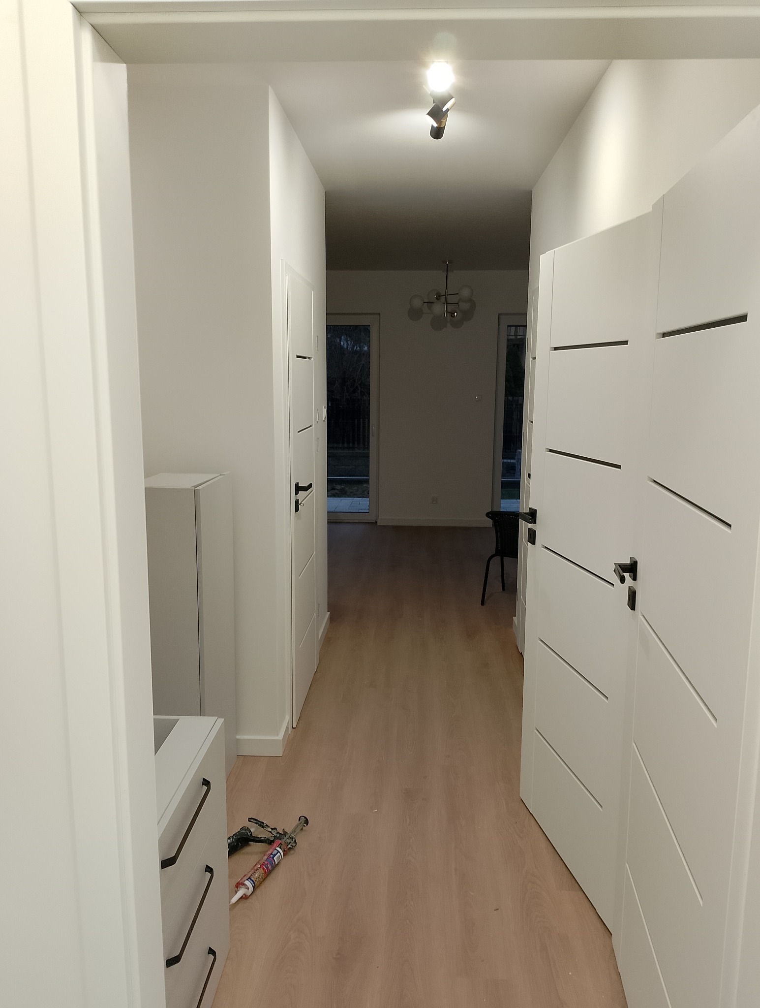 Korytarz po remoncie z białymi drzwiami z poziomymi frezami, jasną podłogą i widocznymi narzędziami do montażu listew przy podłodze.