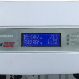 Biała obudowa inwertera SolarEdge z wyświetlaczem LCD pokazującym dane produkcji energii: 10.3 kWh dziennie, 333.7 kWh miesięcznie, 21.258 MWh rocznie i 41.635 MWh łącznie. Świeci się zielona dioda...