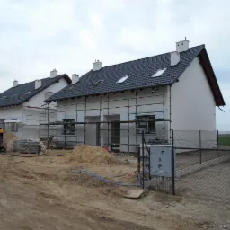 Domy jednorodzinne w Gortatowie w trakcie ocieplania elewacji, widoczne rusztowania i materiały budowlane na placu budowy.