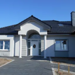 Nowoczesny dom jednorodzinny z szarą elewacją, grafitowym dachem i brukowanym podjazdem w miejscowości Września.