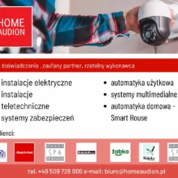 Mężczyzna w koszuli w kratę trzyma w dłoni kamerę IP, widoczny fragment ściany i gniazdko elektryczne, u góry logo firmy HOME AUDION, lista usług i logotypy klientów.