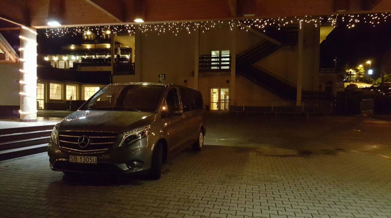 Szary Mercedes Vito z numerem rejestracyjnym SB 1305U zaparkowany nocą przed budynkiem z dekoracyjnym oświetleniem.