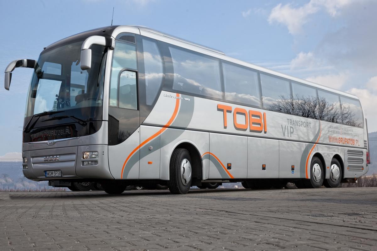 Srebrny autokar MAN Lion's Coach z pomarańczowymi akcentami i logo TOBI Transport VIP na tle błękitnego nieba