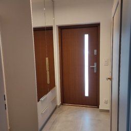 Nowy Wymiar Mebli - Wnętrze przedpokoju z szafą wnękową z lustrami i brązowymi drzwiami wejściowymi z pionowym przeszkleniem, szare płytki podłogowe.