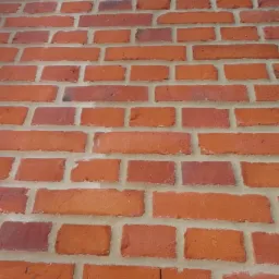 Czerwona ściana z cegły, ułożona w regularny wz&oacute;r. Widoczne spoiny wypełnione jasną zaprawą. Ujęcie pod kątem.