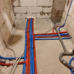 INSTAL-EXPERT - Nowa instalacja wodna z rurami w kolorze niebieskim i czerwonym, zabezpieczonymi pianką montażową, w surowym wnętrzu budynku z bloczków.