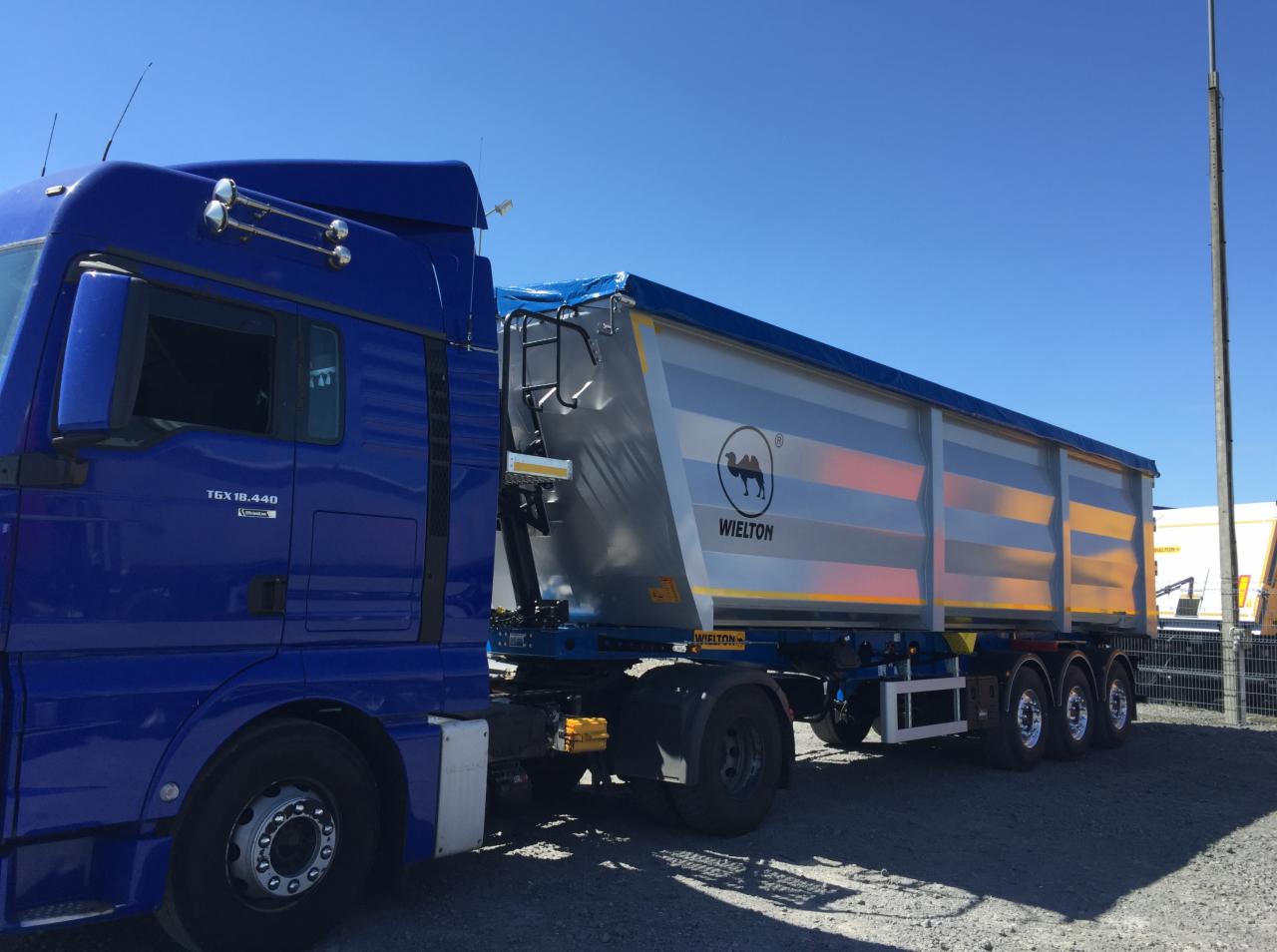 Niebieski ciągnik siodłowy MAN TGX 18.440 z naczepą wywrotką Wielton z logo wielbłąda na tle błękitnego nieba.